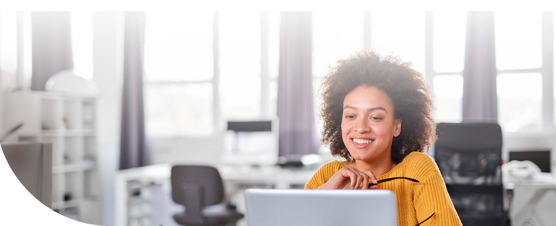 mujer afrodescendiente sonriendo y observando su computadora en la oficina